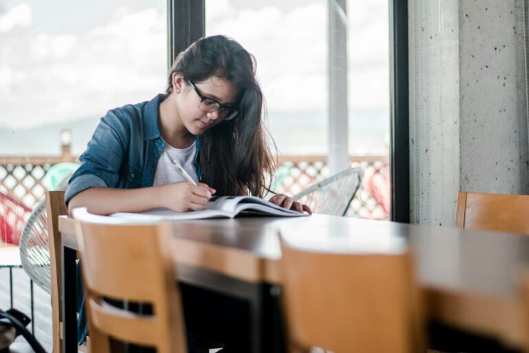 A student writing notes beside an open book