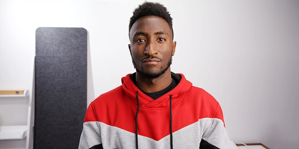 Marques Brownlee in a red and grey hoodie in a studio.
